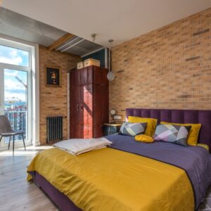 Bright contemporary bedroom with purple and yellow decor, brick wall, and cityscape view.